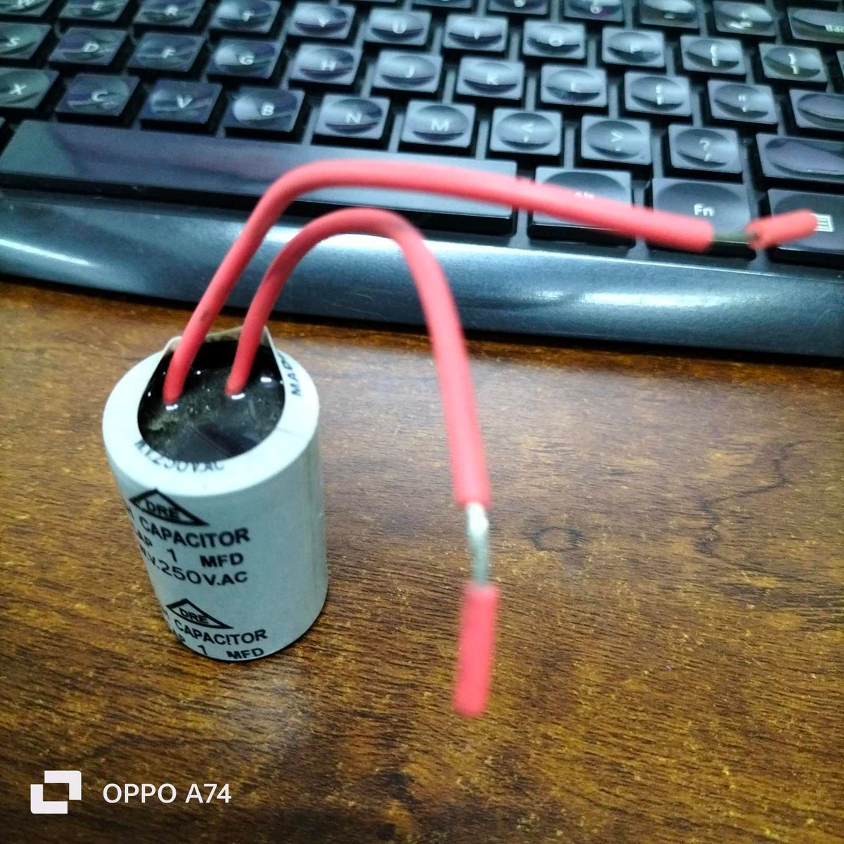 DRE 1MFD 250V AC motor running capacitor with red wires on a wooden surface