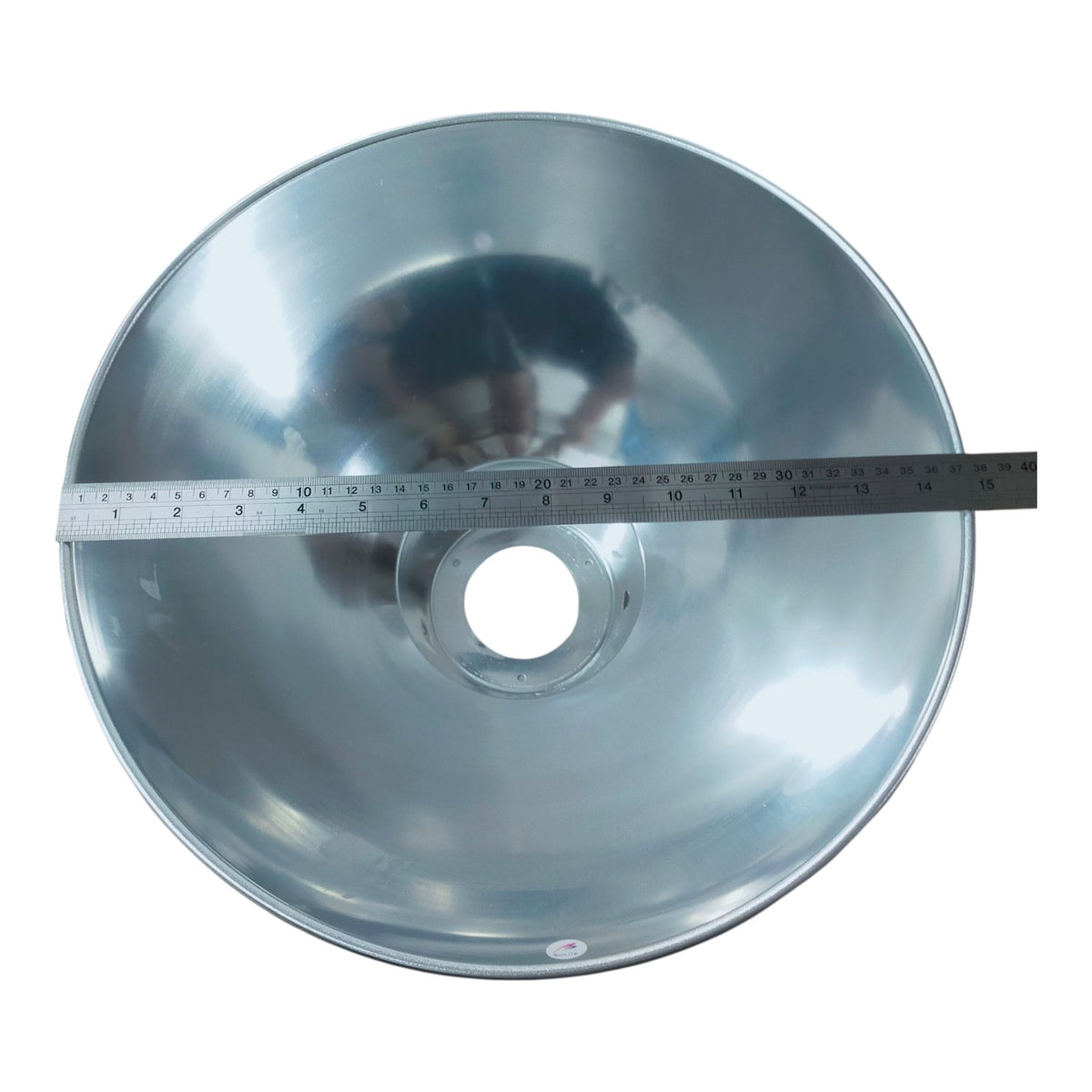 A large silver metal dome-shaped reflector with a circular center hole, shown with a metal ruler laid horizontally across the middle to indicate size, on a plain white background.
