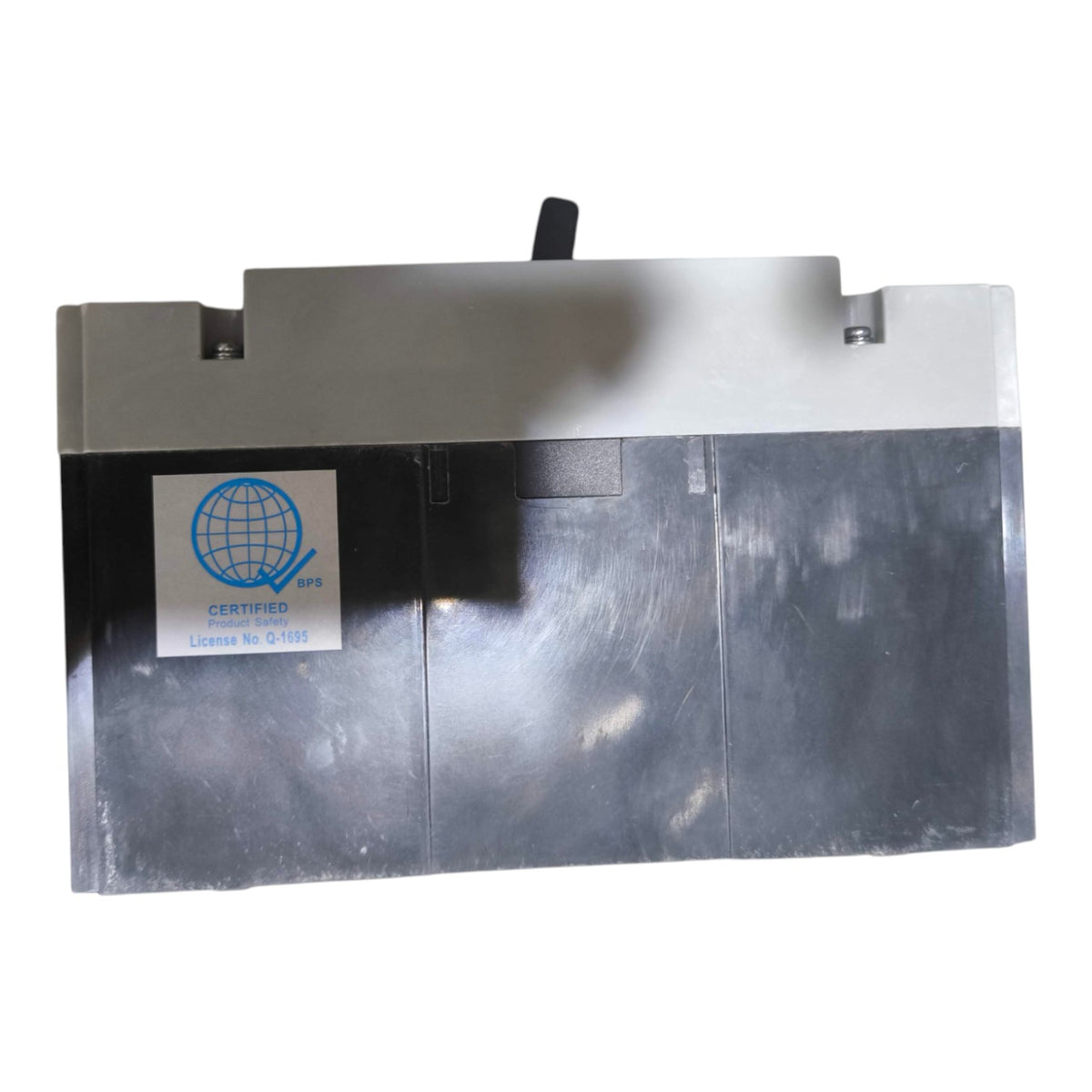 A rectangular metallic industrial component or enclosure with a brushed silver finish, featuring a white certification sticker on the front left and a small black handle or rod protruding from the top center, shown against a plain white background.