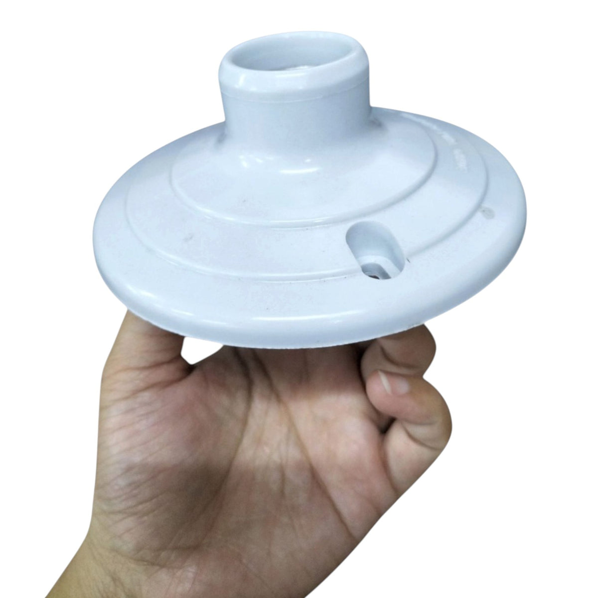 A hand holding a white plastic light fixture canopy against a plain white background.