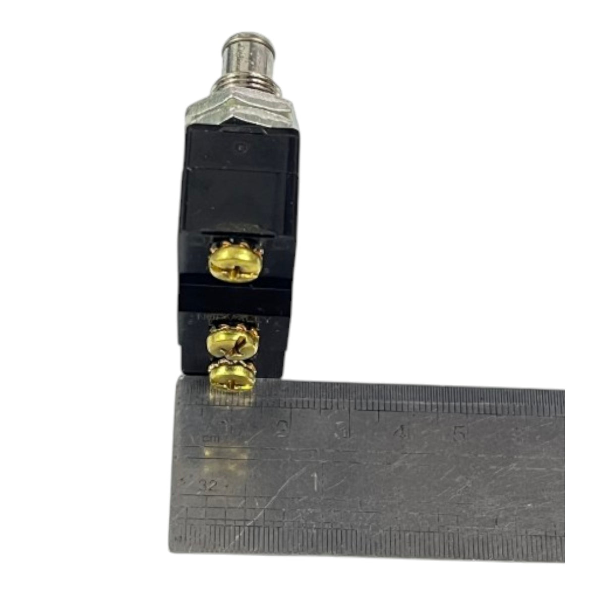 A small black electrical component with gold screw terminals and a silver metal top, shown next to a metal ruler for scale on a white background.