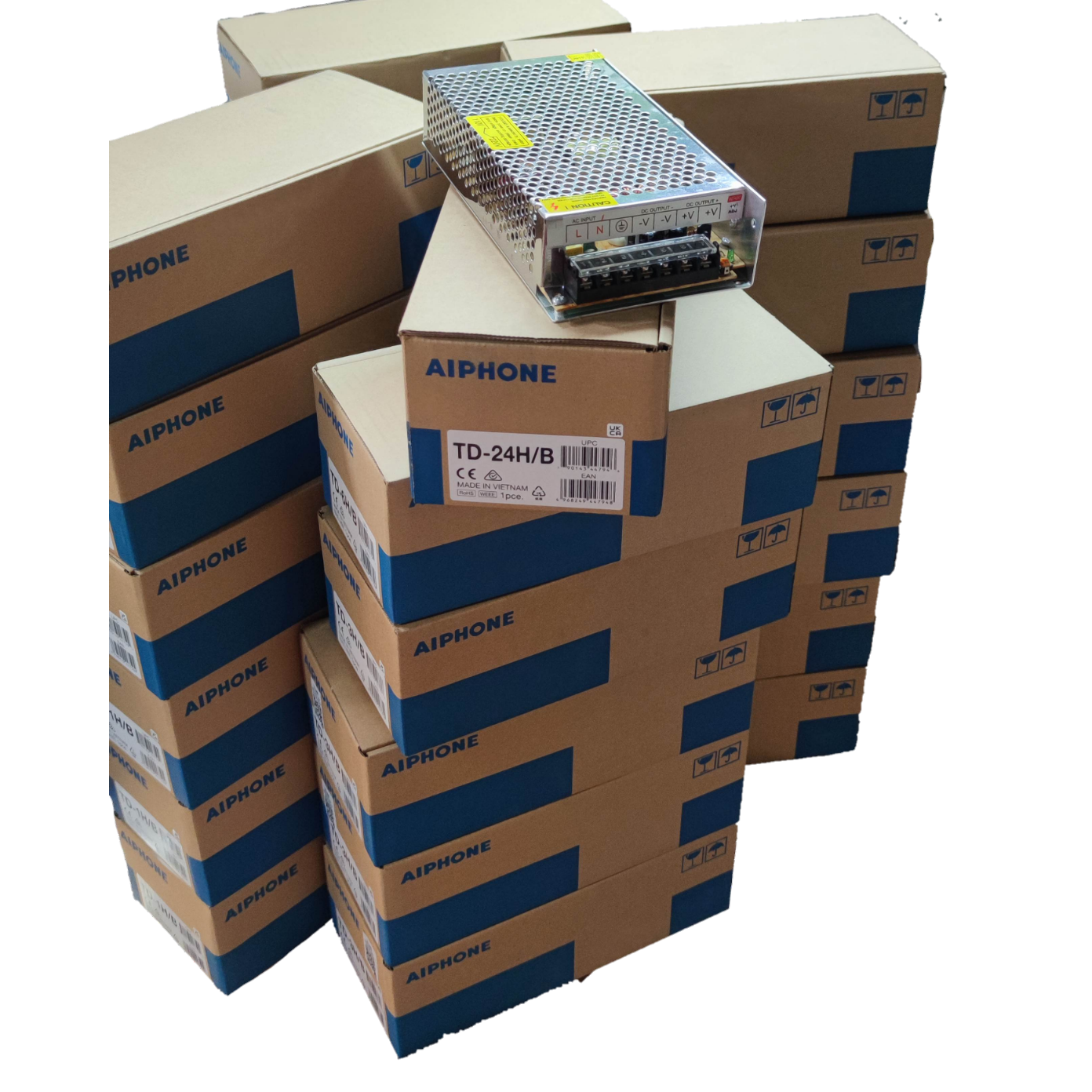 Aiphone 24 station intercom system components stacked in labeled boxes with a metal power supply unit on top