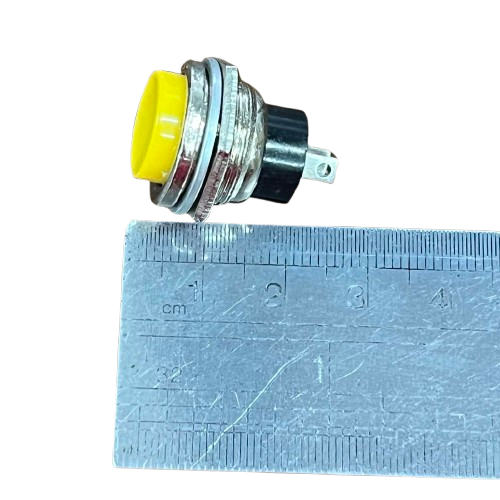 Push Button Switch 1A 220V Yellow with a Metal Base and Mounting Pins Next to a Ruler for Size Reference