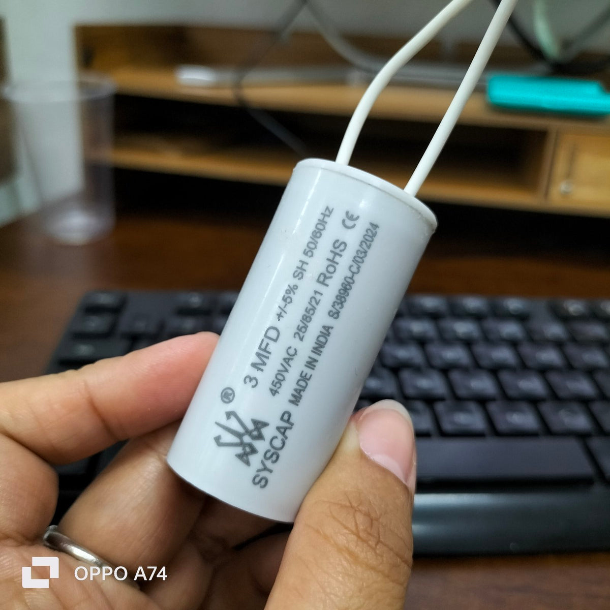 Syscap 3MFD 450V AC Running Capacitor held in hand with keyboard and desk background