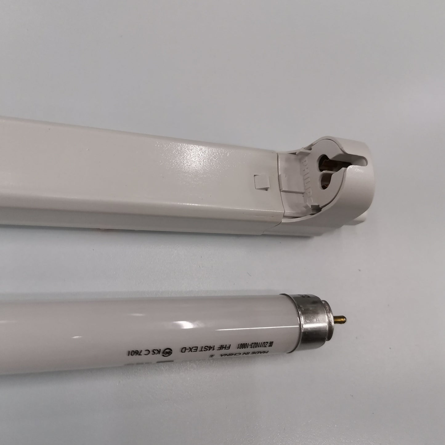 Philips T5 Fluorescent Lamp 28 Watts Daylight tube next to white lamp fixture on a white surface