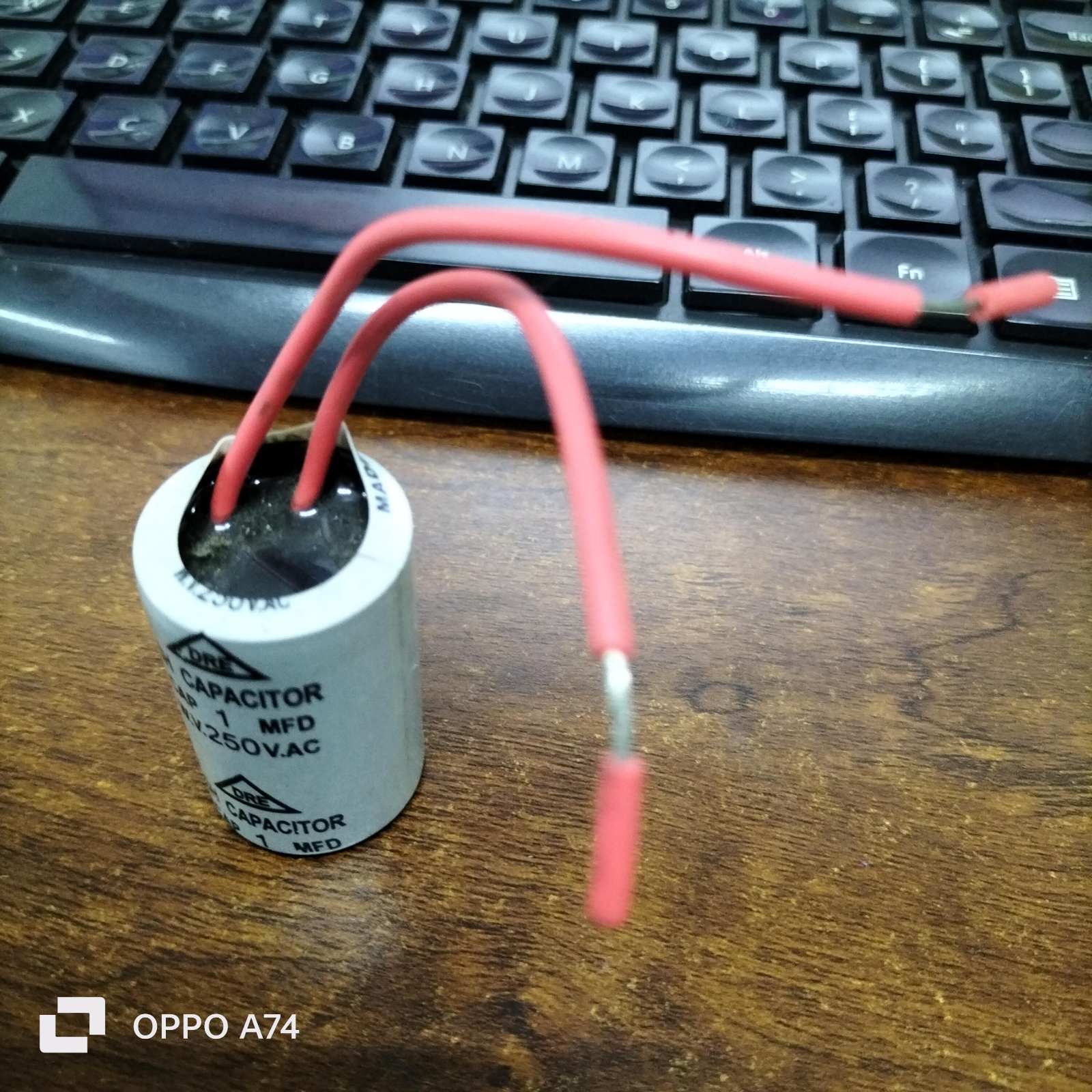 DRE 1MFD 250V AC motor running capacitor with red wires on a wooden surface