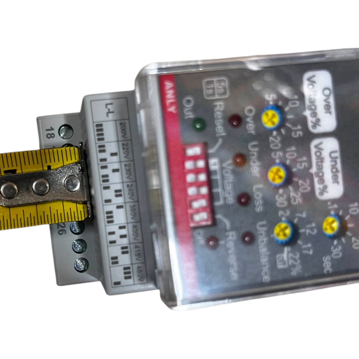 A close-up of an electrical monitoring device with a clear plastic housing, showing LED indicators, labels for over/under voltage and percentage, and a yellow measuring tape attached to the terminal block.