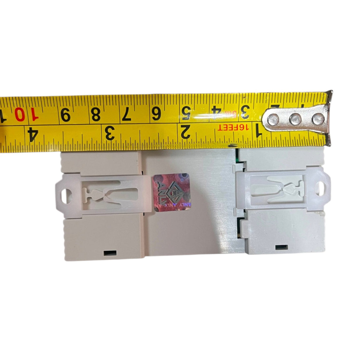 A white plastic electrical outlet or switch component shown against a white background, with a yellow tape measure placed above it for scale.