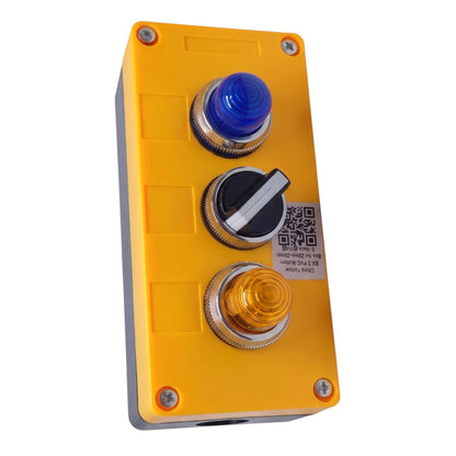 A yellow industrial control panel box with three circular push buttons: a blue button at the top, a black-and-white toggle in the middle, and an amber button at the bottom. The panel is secured with four corner screws and has a white label on the right side with a QR code and technical text.