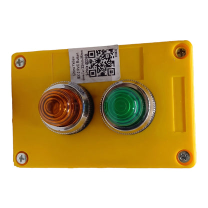 A yellow industrial control panel featuring a dual-button switch. The left button has a clear amber lens, and the right button has a green lens.