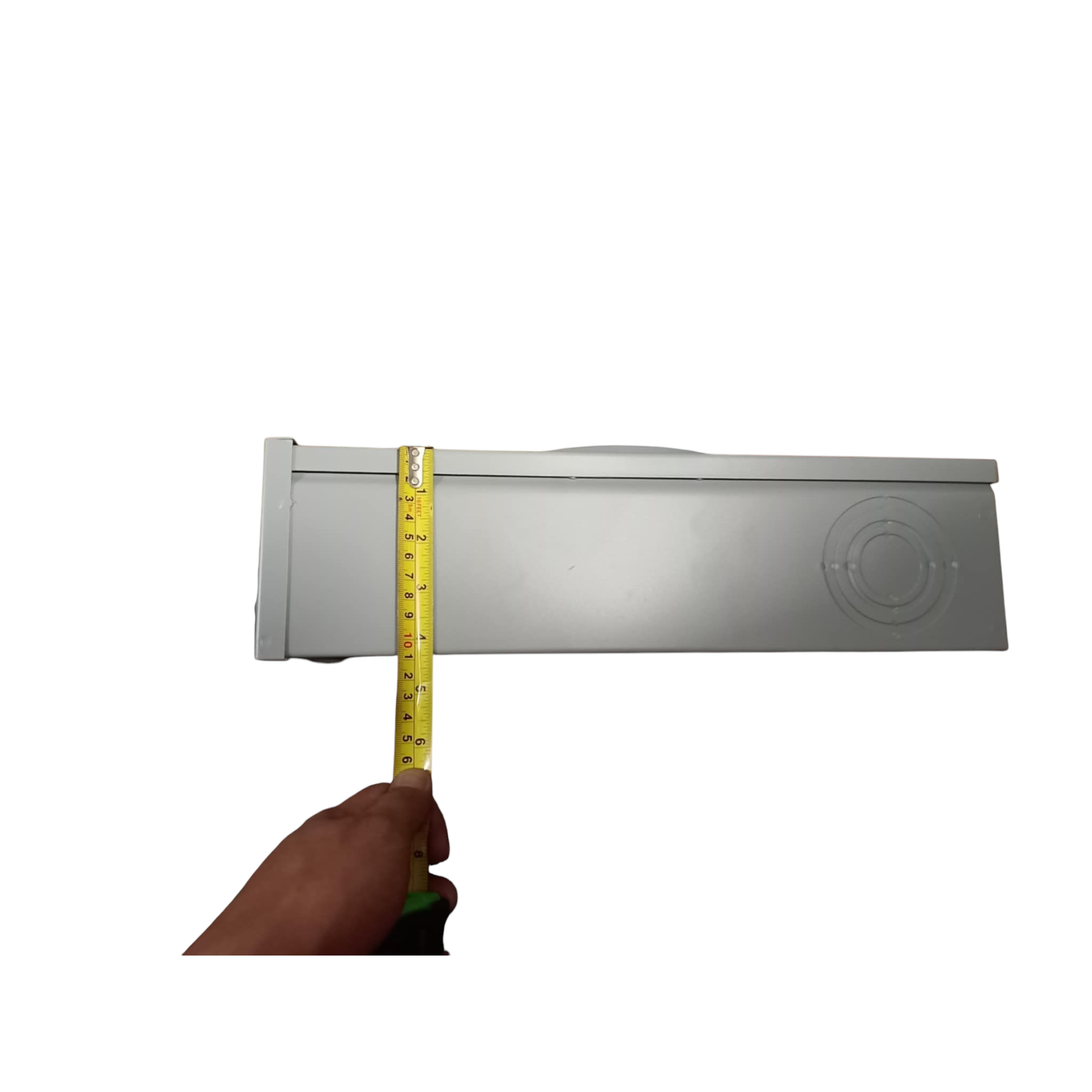 Hand holding a measuring tape against a rectangular metal object on a white background