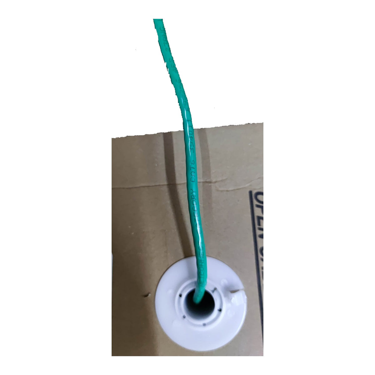A close-up of a green wire or cord inserted into a white circular plastic spool mounted on a brown cardboard backing against a white background.