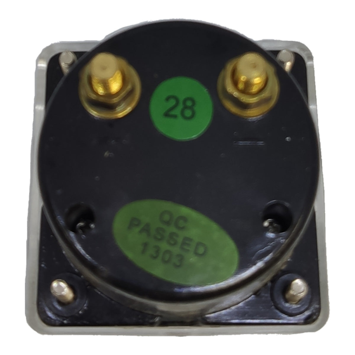 A square metal electrical component with a black circular top plate, two gold screw terminals, and green stickers reading '28' and 'QC PASSED 1303'.