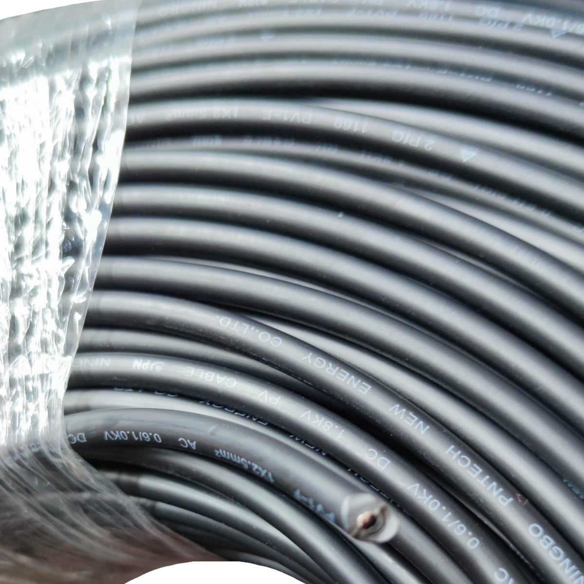 A close-up of a large spool of black industrial cable wrapped in clear plastic, with printed white text showing specifications such as 'PHITECH', 'ENERGY', '3M', and '0.6/1.