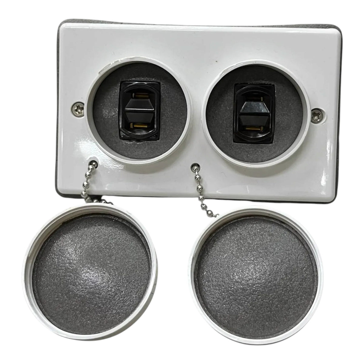 A white rectangular electrical outlet cover plate with two circular openings, each containing a black switch, shown with two round gray mesh caps hanging below by short metal chains on a white background.