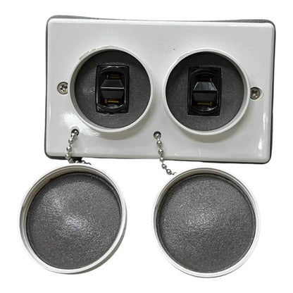 A white rectangular electrical outlet cover plate with two circular openings, each containing a black switch, shown with two round gray mesh caps hanging below by short metal chains on a white background.