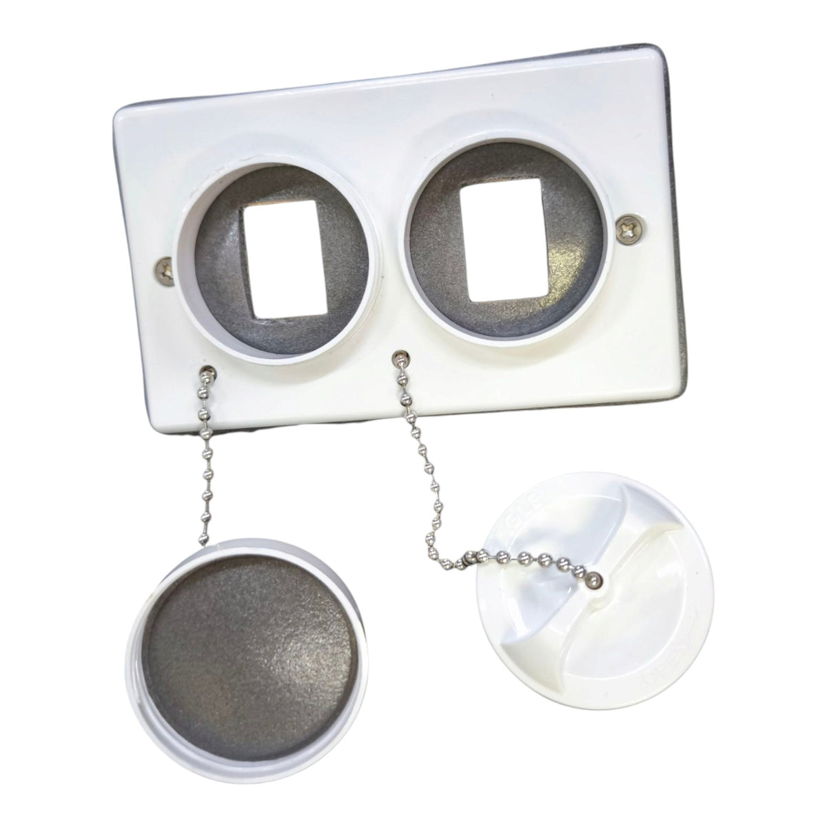 A white plastic dual-sink drain assembly with two circular openings, shown with the lower drain caps and chain detached below on a plain white background.