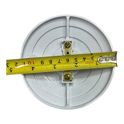A circular white electrical junction box with two brass screw terminals, shown with a yellow tape measure stretched horizontally across the center to indicate dimensions, on a plain white background.