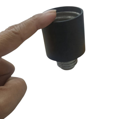 A hand holding a black cylindrical plastic cap with a threaded metal bottom against a plain white background.