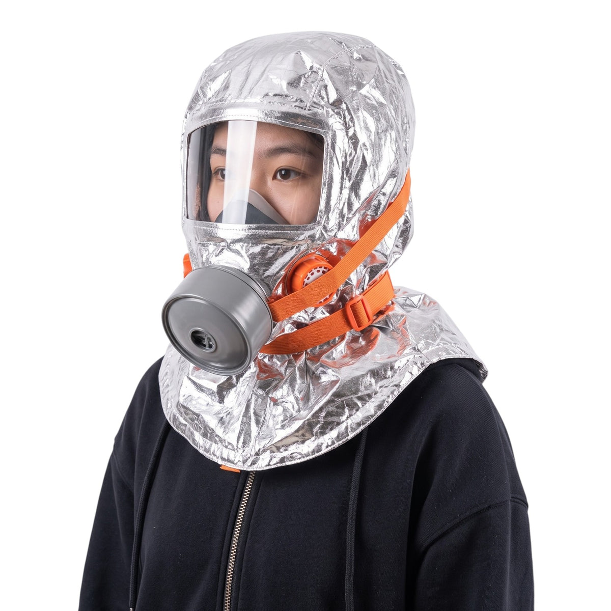 A person wearing a reflective silver foil hooded face shield with a clear visor, orange straps, and a gray respirator mask, over a black zip-up hoodie against a white background.