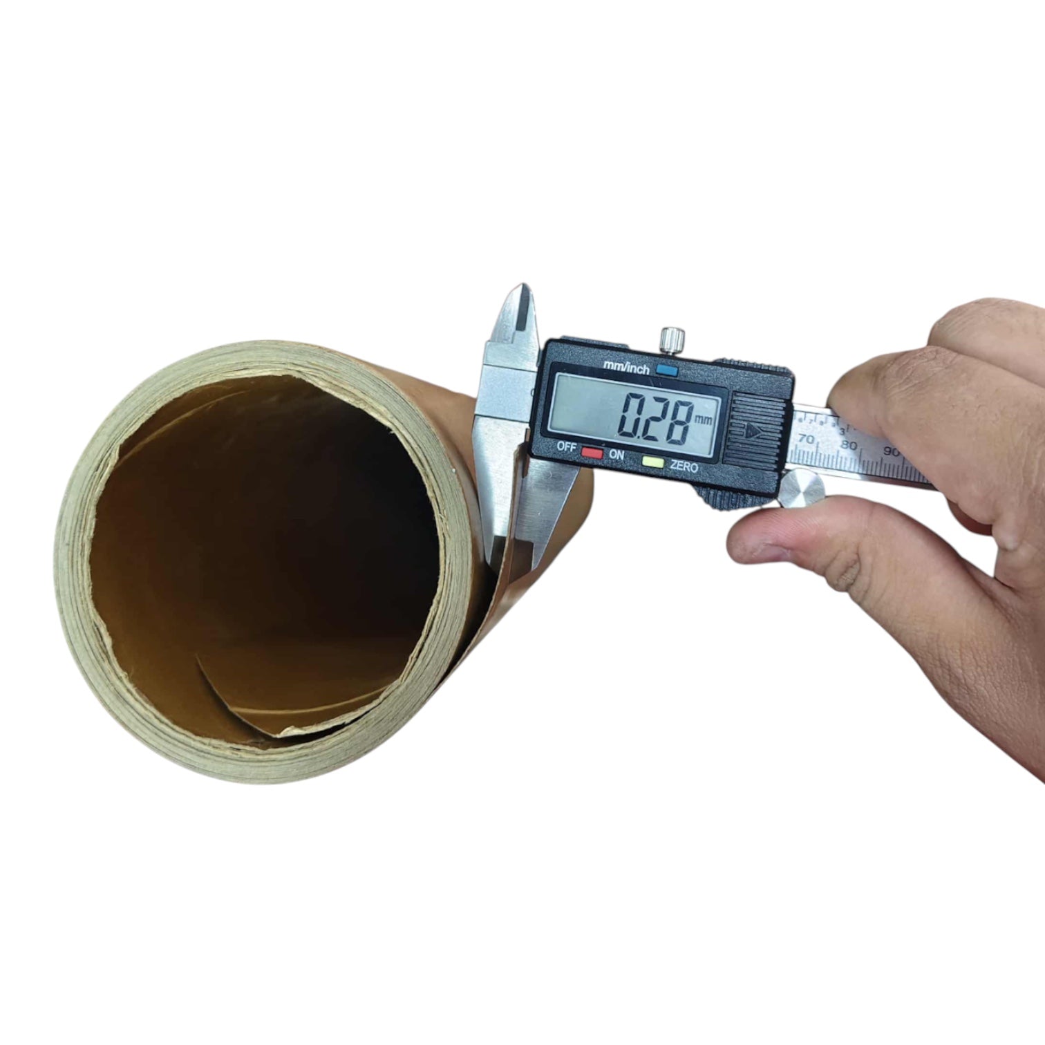 A hand holding a digital caliper measuring the thickness of a roll of brown kraft paper or cardboard on a plain white background.