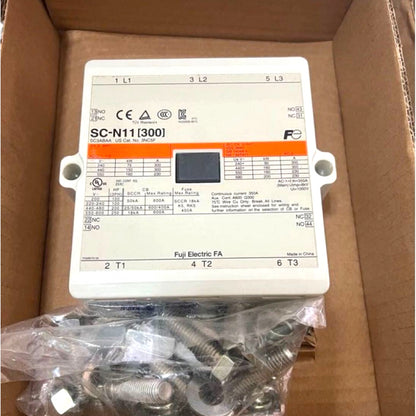 A Fujitsu Electric SC-N11[300] electrical fuse holder box with a small display screen, shown inside its cardboard box packaging with mounting hardware below.