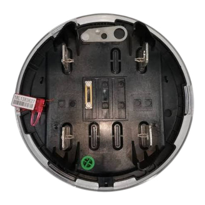 Top-down view of a circular black electrical compartment or battery terminal housing with metal terminals, a small red wire with a white tag, and a green plastic insert near the bottom, isolated on a white background.