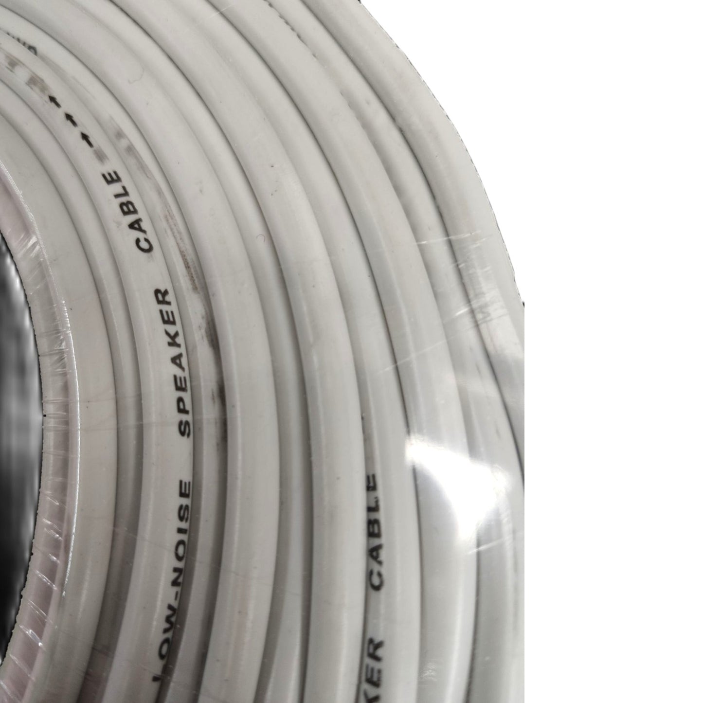 A close-up of a coiled white speaker cable wrapped in clear protective plastic, with black printed text reading 'LOW-NOISE SPEAKER CABLE'.