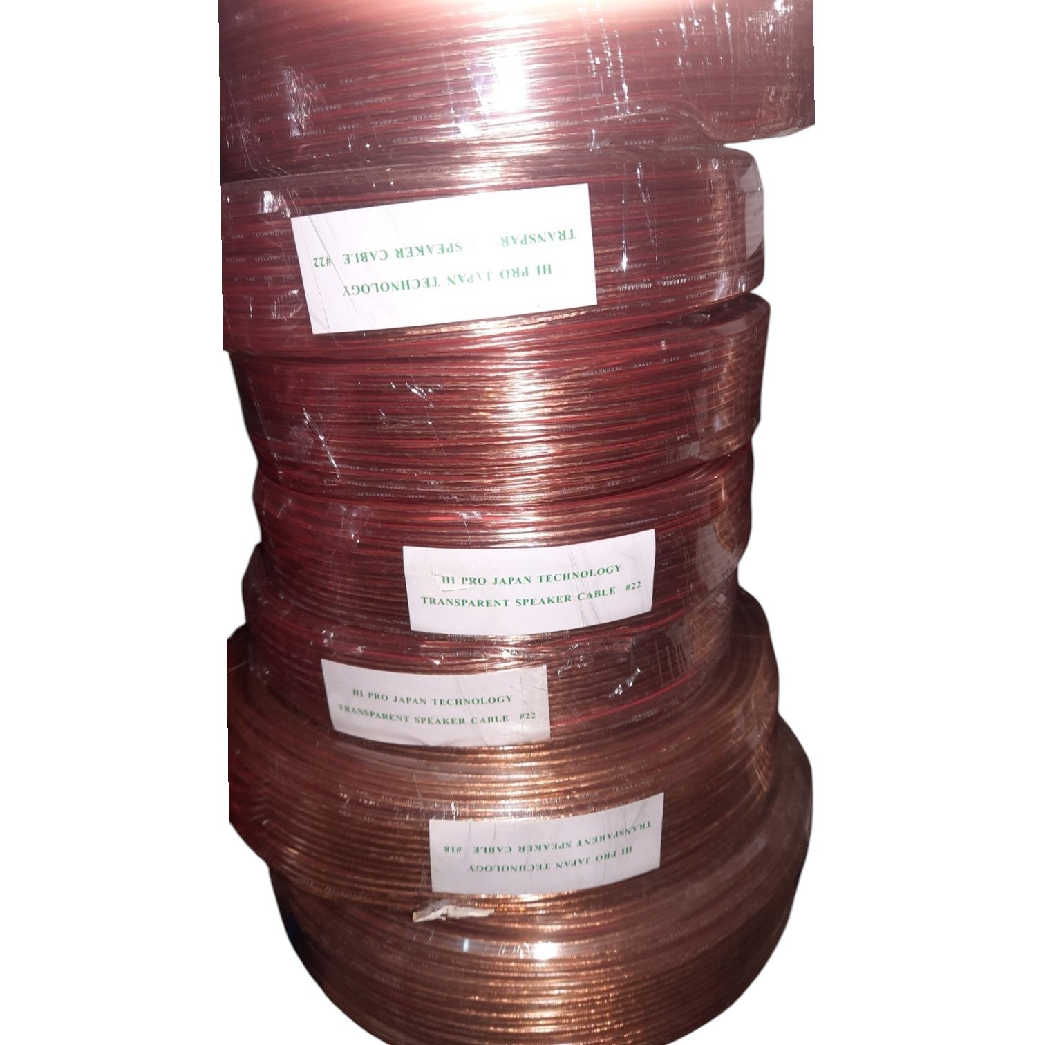 A stack of copper-colored speaker wire spools wrapped in clear plastic, with white labels showing text including 'III PRO JAPAN TECHNOLOGIES' and 'TRANSMITTER SPEAKER CABLE'.