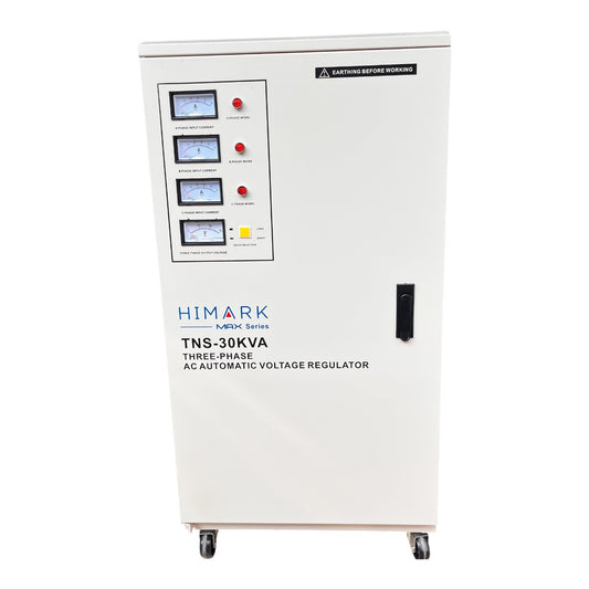 A white HIMARK TNS-30KVA three-phase AC automatic voltage regulator cabinet on wheels, featuring a front panel with multiple analog meters, red emergency stop buttons, and a black warning label.