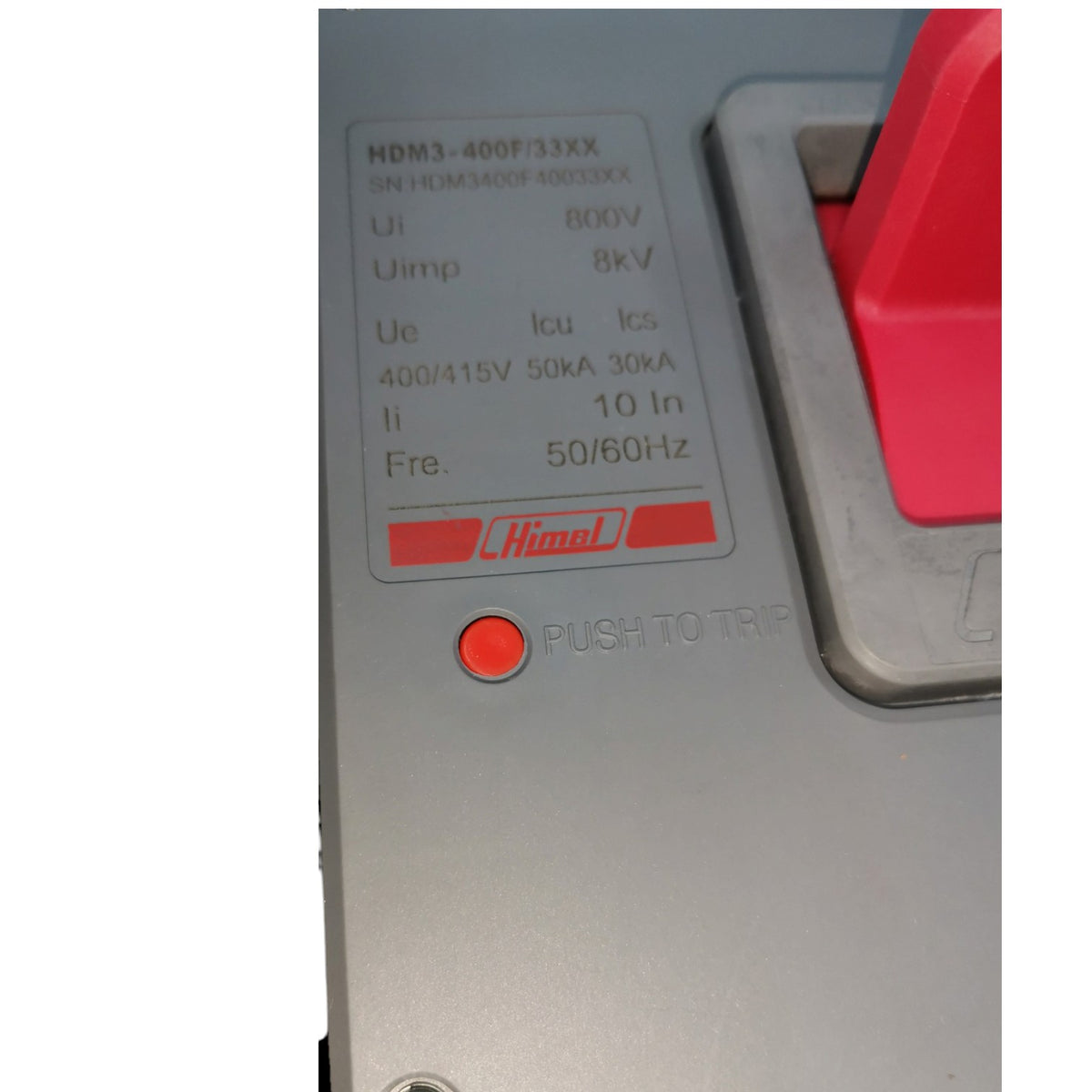 Close-up of a Himo electrical circuit breaker panel showing technical specifications, a red push-to-trip button, and part of a red handle on a gray housing.