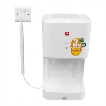A white countertop electric kettle with a transparent water reservoir and a power cord plugged into a wall outlet, shown on a plain white background.