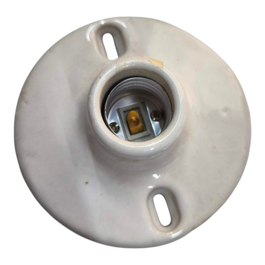 A round ceramic light socket base with a central threaded contact point and two mounting slots, shown on a plain white background.