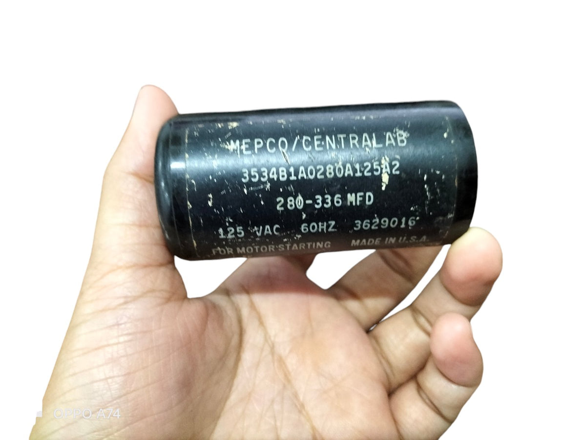Hand holding a black motor starting capacitor 280-366 MFD electrical part from China