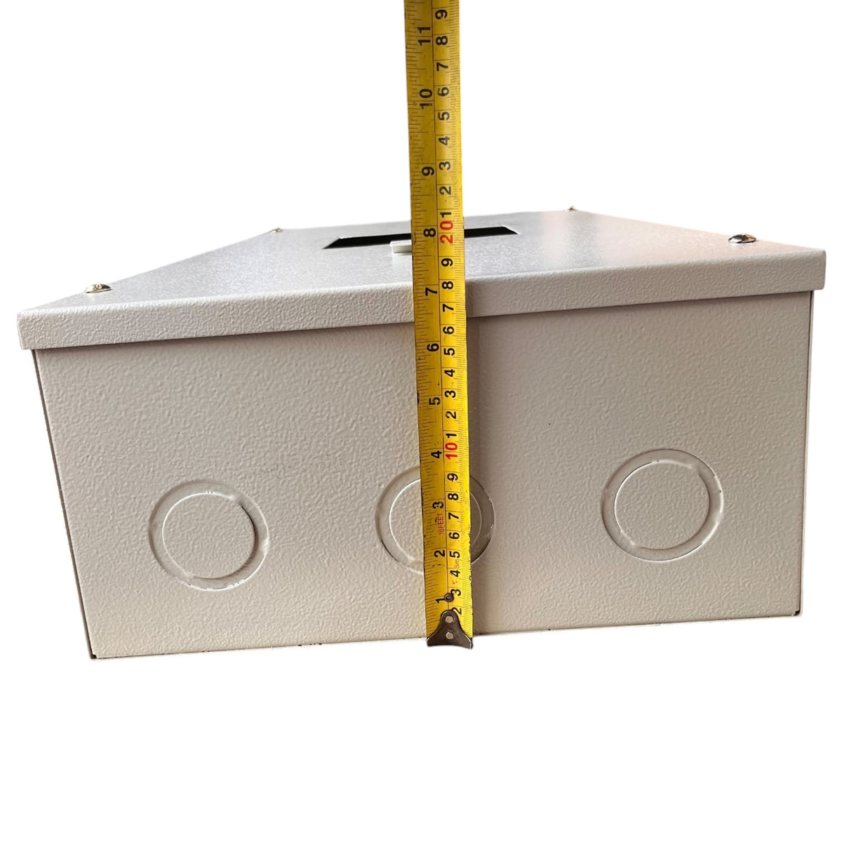 A light gray metal junction box with circular terminal holes on the front, shown with a yellow tape measure standing vertically to indicate its height against a plain white background.
