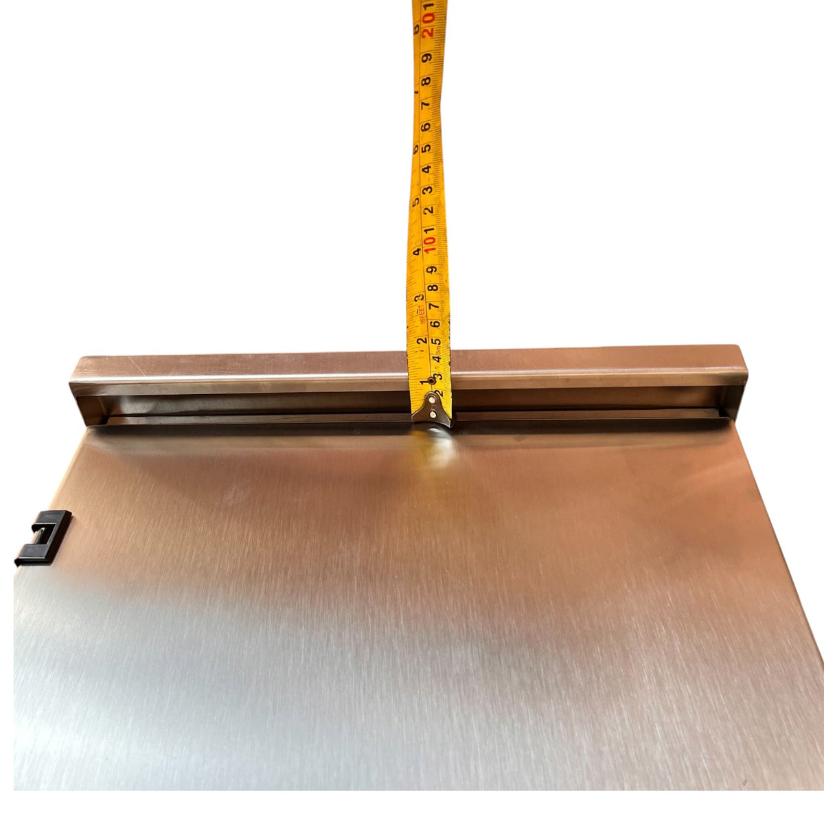 A brushed metal rectangular panel with a brass-colored mounting bracket and a yellow tape measure standing vertically against the top edge, shown on a plain white background.