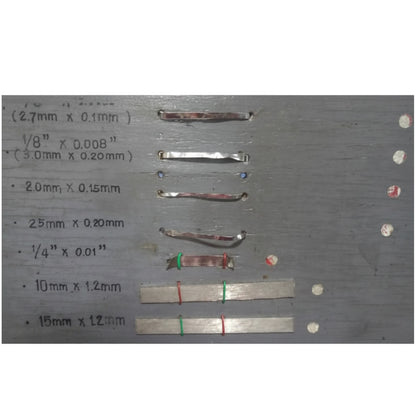 A gray metal sample board with handwritten size measurements in millimeters and inches next to several small strips of metallic material, likely showing material samples by size.