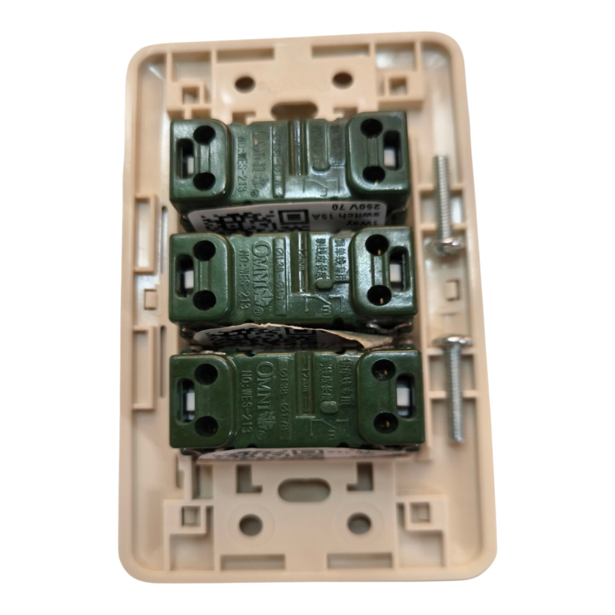 A top-down view of a beige electrical switch plate cover with three green OMNI brand junction blocks and mounting screws inside, isolated on a white background.