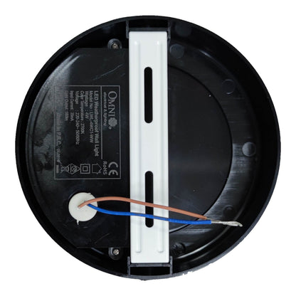 Top-down view of a circular black LED motion sensor light fixture base, showing internal wiring with blue and copper wires connected to a white terminal, and a white mounting bracket in the center.