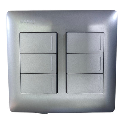 A square metallic silver 6-way light switch plate with two columns of three individual switches, featuring a brushed metal texture and a subtle brand engraving in the top left corner.
