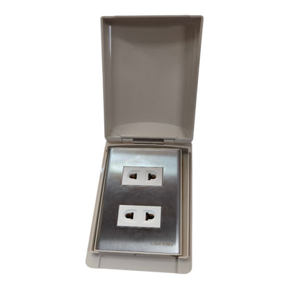 A waterproof double outlet socket cover with a hinged lid, featuring a brushed stainless steel faceplate with two UK-style three-pin sockets and a beige plastic outer casing.