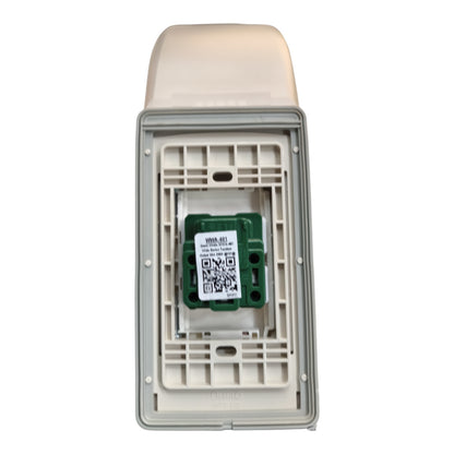 An outdoor electrical outlet cover with a beige plastic top and a gray plastic frame, showing the interior mounting plate and a green electronic component with a QR code label.