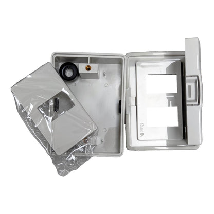 A white plastic electrical junction box or enclosure shown open on a white background, with a separate clear plastic-wrapped component placed beside it. The inside of the box is visible and appears empty or partially assembled.
