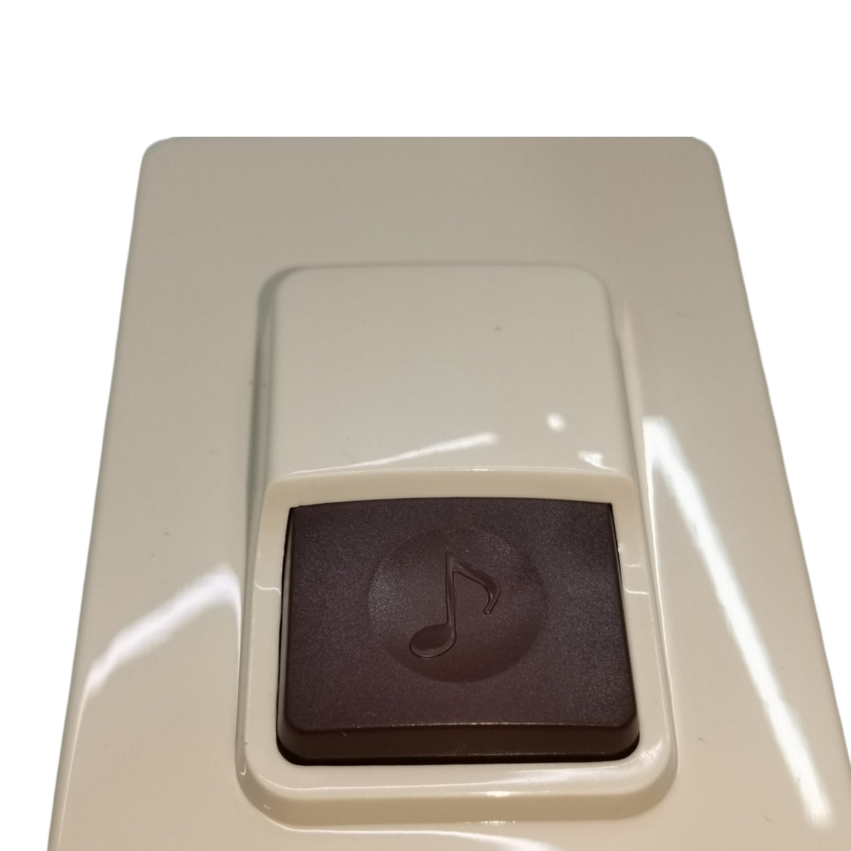 A close-up of a beige electronic control panel featuring a recessed square button with a dark brown face and an embossed music note symbol.