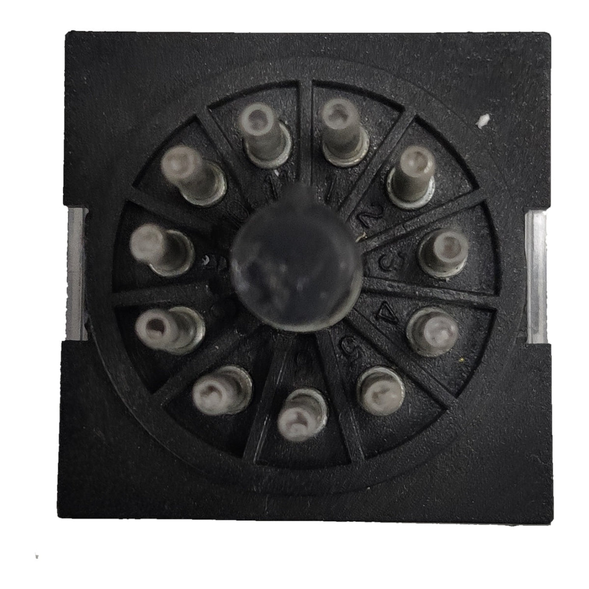 A black circular multi-pin electrical connector or terminal block with a central round knob and multiple small metal pins radiating outward, shown on a plain white background.