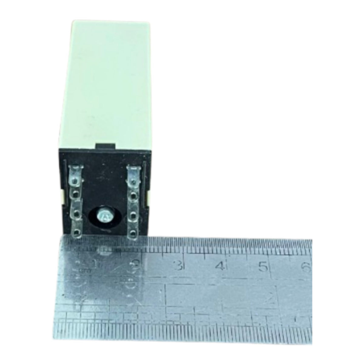 A small rectangular electronic component with a black front and pale green top, shown next to a metal ruler for scale on a white background.