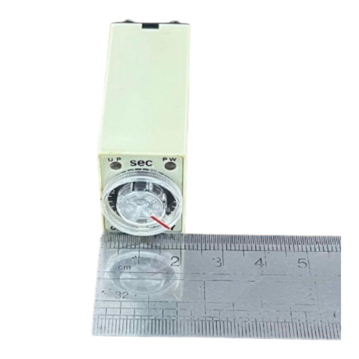 A small rectangular electronic timer or switch with a round dial and printed labels, shown upright next to a metal ruler on a white background.