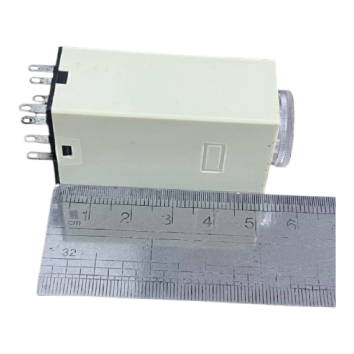 A small rectangular electrical switch or relay component with multiple metal pins on one side and a translucent end cap, shown next to a metal ruler for scale on a white background.