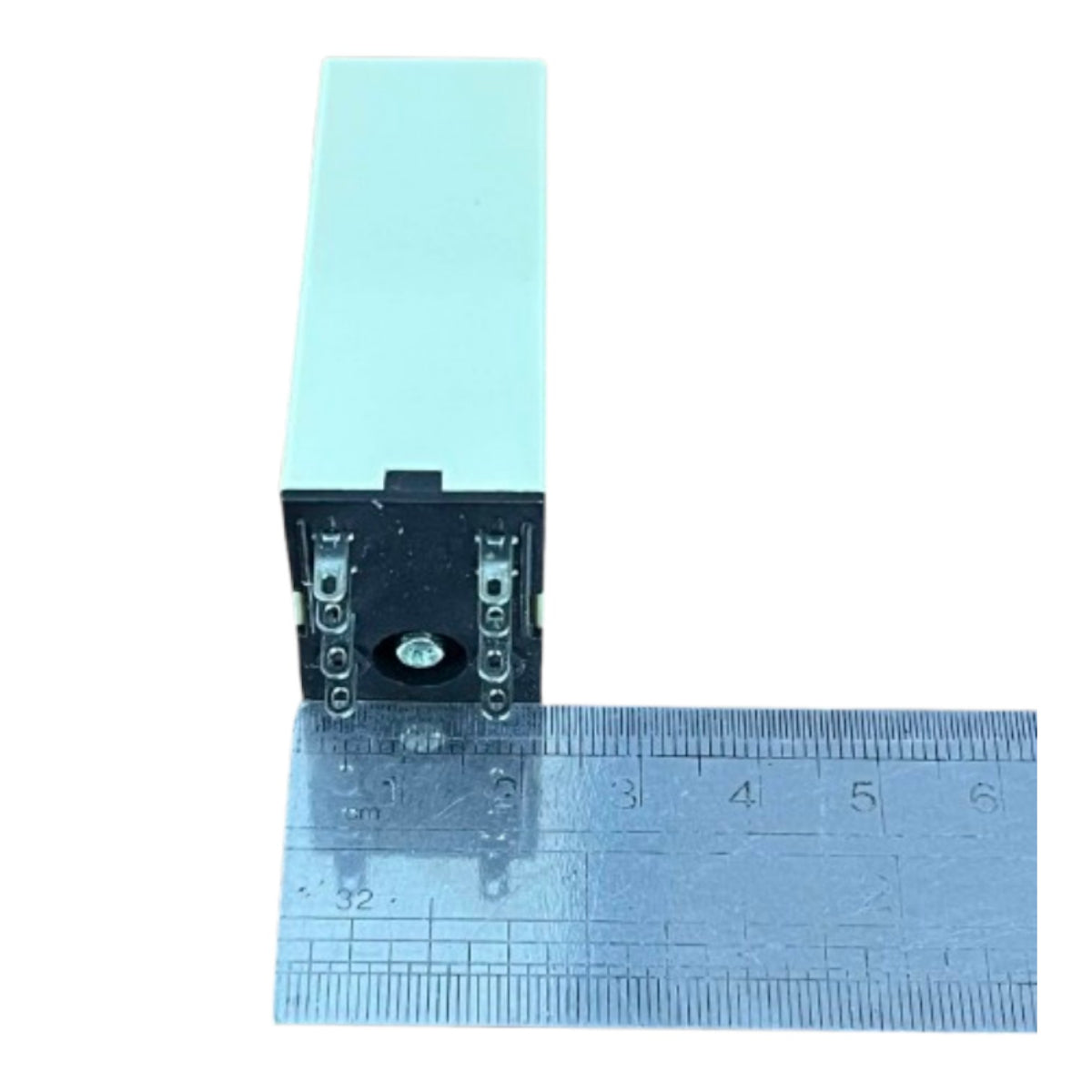 A small rectangular electronic component with a pale mint-green top and black side, shown next to a metal ruler for scale on a white background.