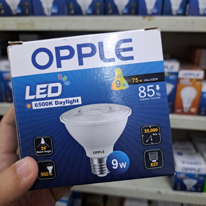 A hand holding an OPPLE 9-watt LED light bulb box in a retail store setting. The box is blue and white with product specifications and an image of the light bulb.